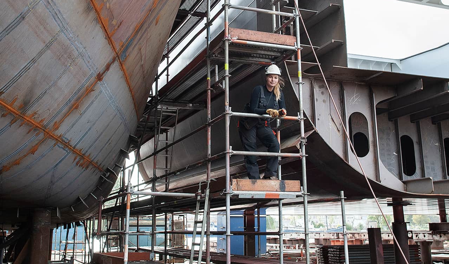 Female working on scaffolding of ship build. 