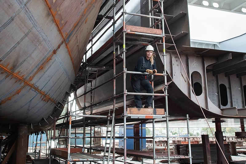 Female working on scaffolding of ship build.