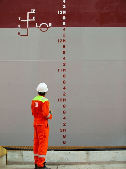 Worker on outside of ship looking at markings. 